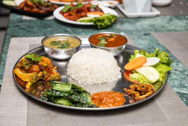 A Nepali thali with rice, dal, curries, greens and pickles on a steel plate